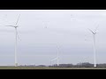 Three white wind turbines in a green field generate renewable energy from the wind