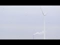 Wind turbine and smoke stack in countryside symbolize green tech and industrial pollution
