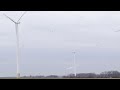 Wind turbines contrast with distant smokestack, symbolizing renewable energy vs pollution
